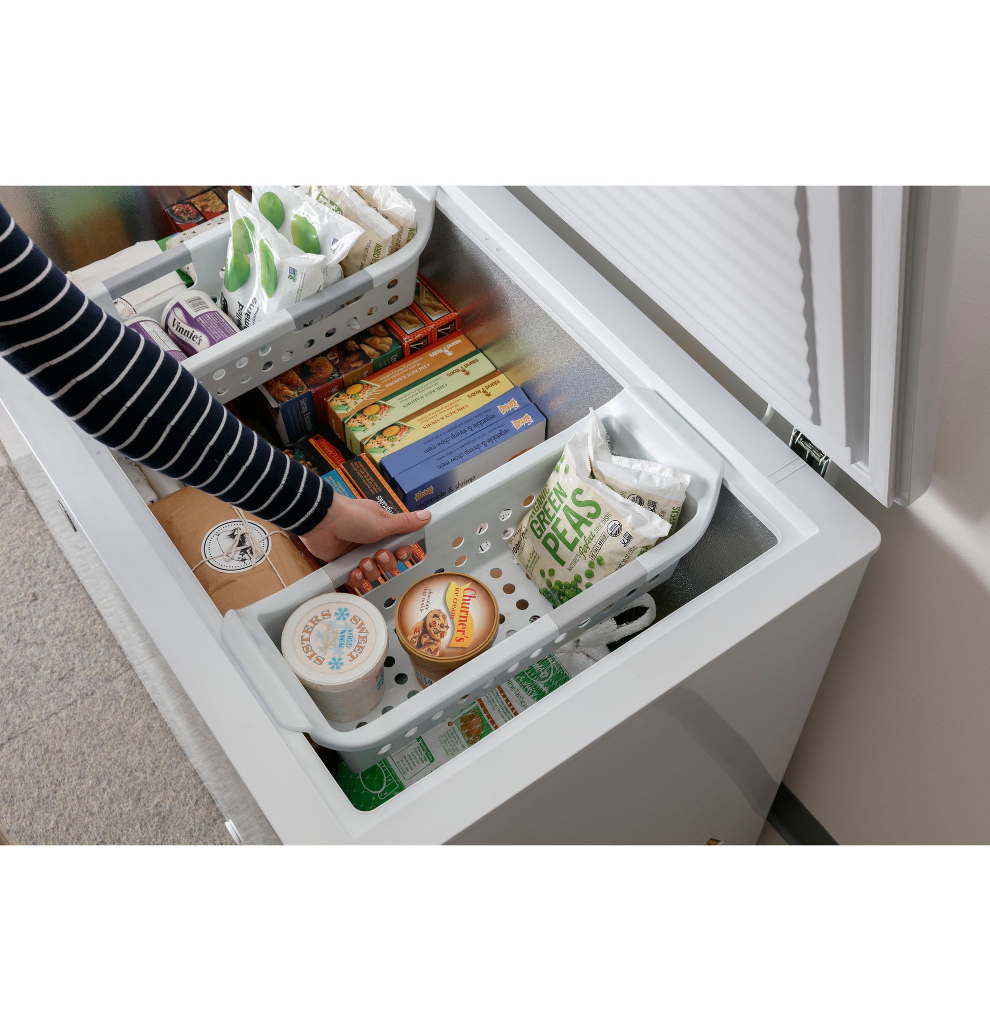 Top interior view of white manual defrost chest freezer with removable basket and assorted frozen food packages inside
