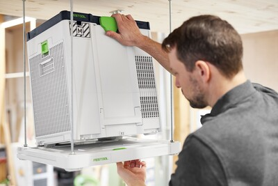 Man adjusting white and green ceiling bracket mounting a Festool air purifier in woodworking tools and dust filtration setup