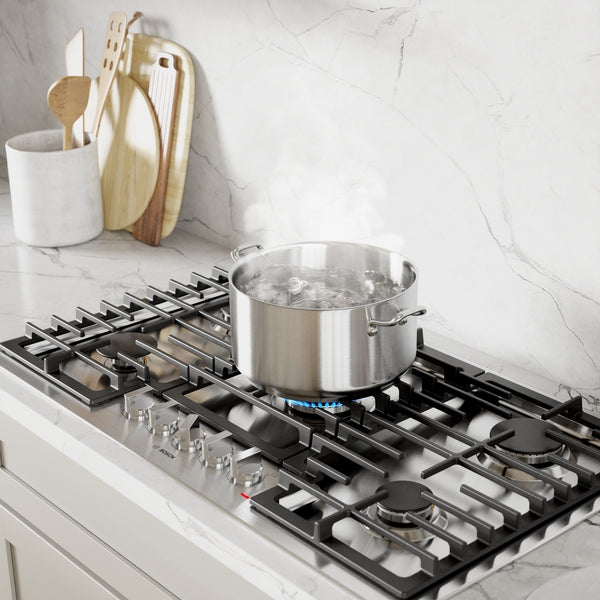 Stainless steel cooktop with boiling pot on gas burner, modern kitchen setting with marble backsplash and utensils container