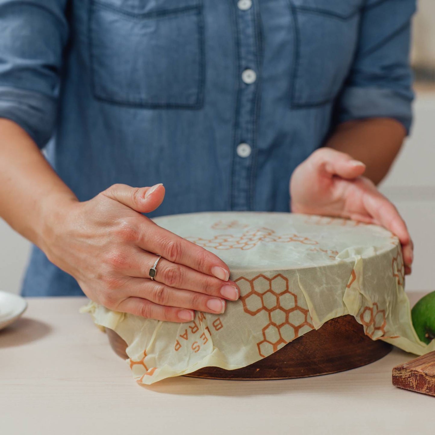 Person covering wooden bowl with large honeycomb-patterned beeswax wrap for kitchen storage under $50 collection