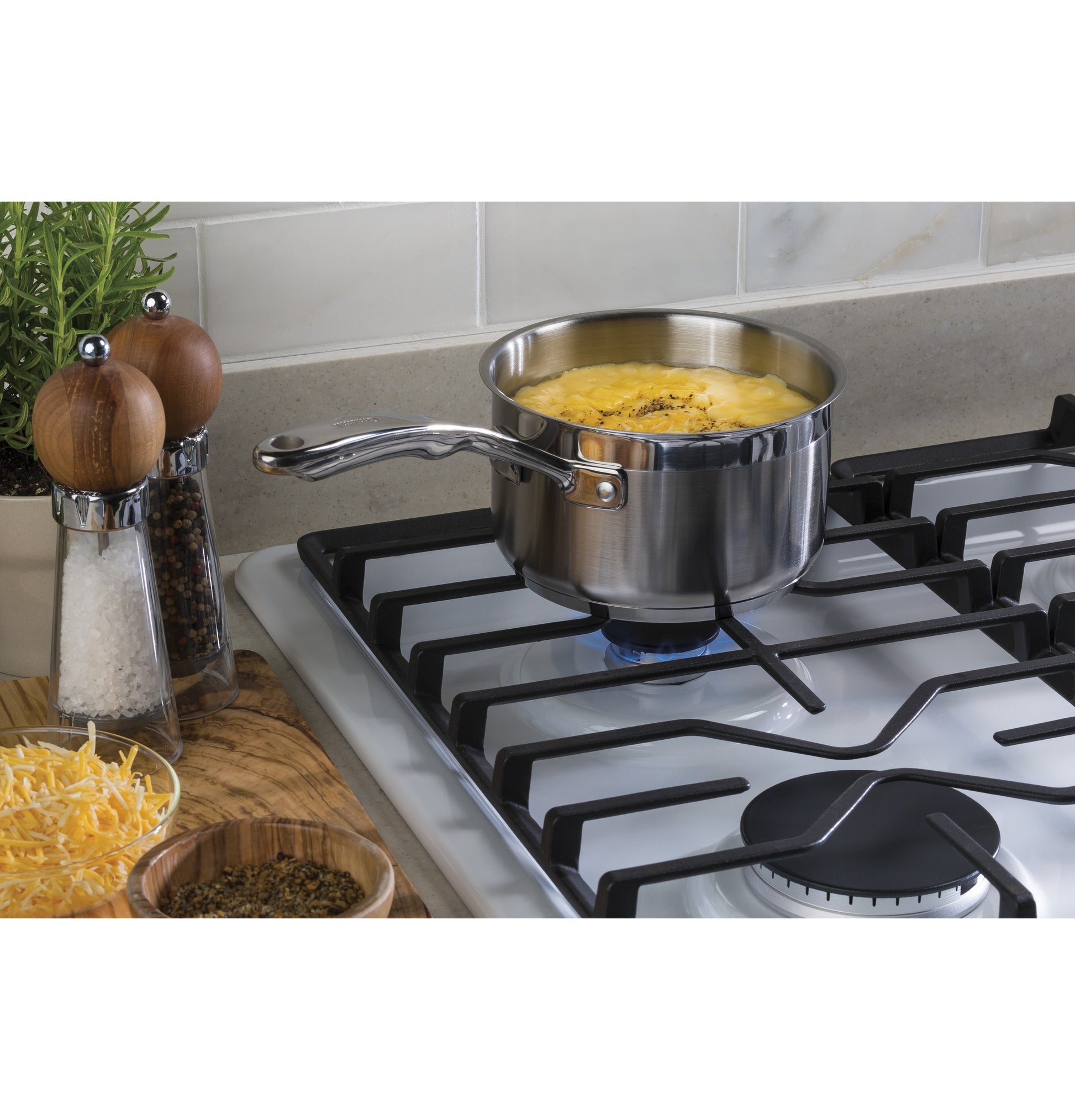 Stainless steel pot cooking over blue flame on white built-in gas cooktop with dishwasher-safe grates in kitchen setting