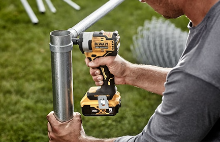 Cordless impact wrench in yellow and black tightening a metal pipe outdoors for home improvement tasks