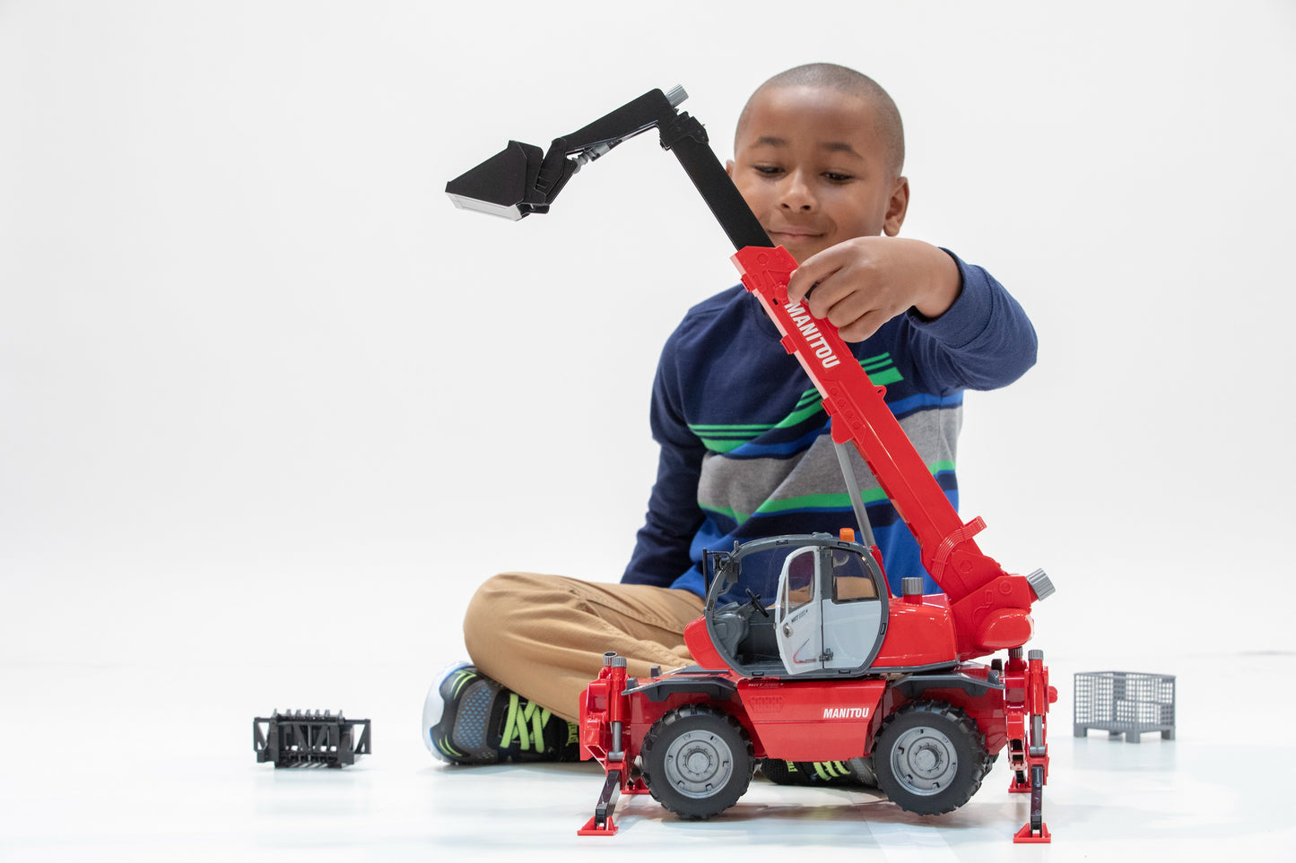 Child playing with red Bruder Toys Manitou telehandler model featuring extendable boom and bucket attachment for imaginative play