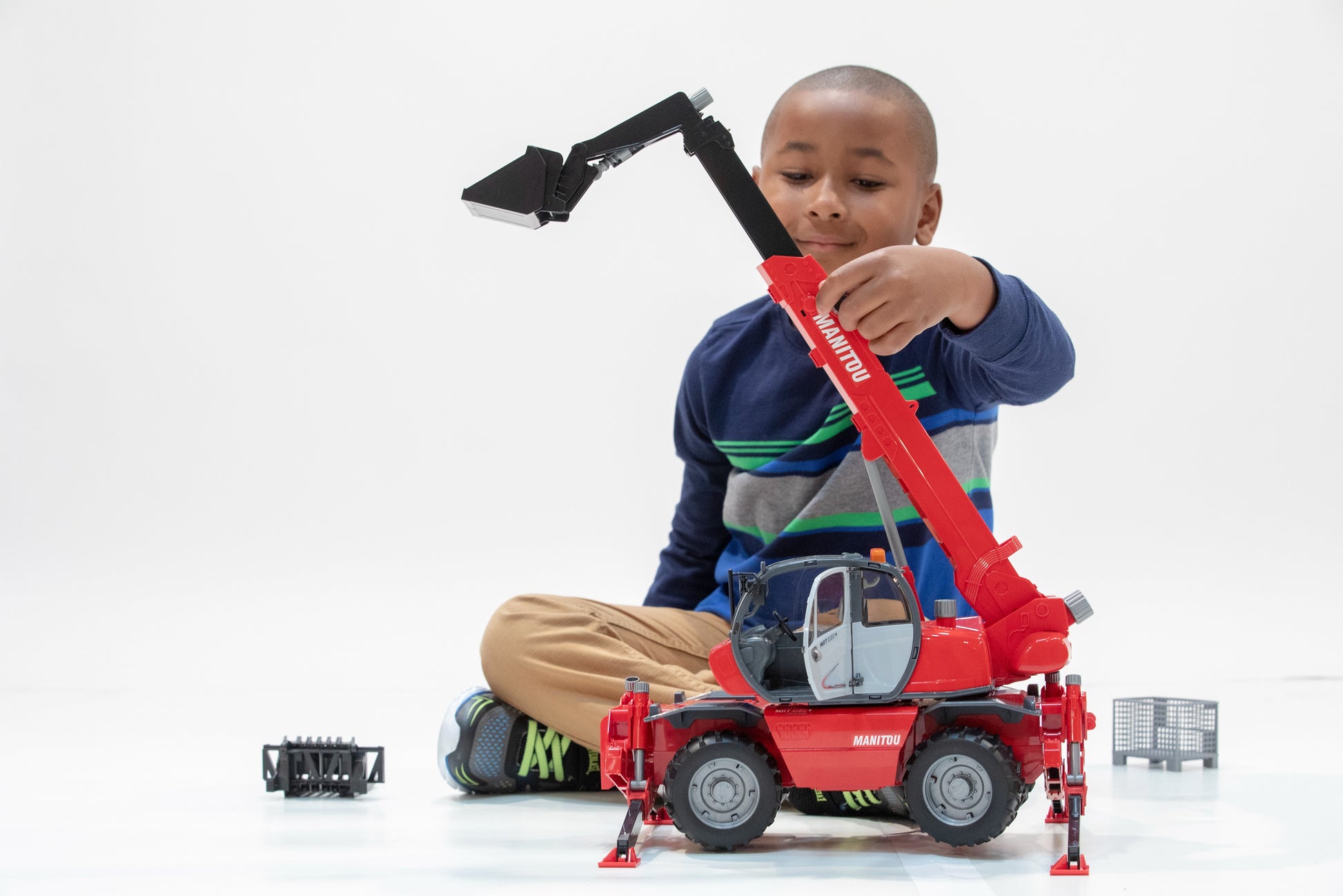 Child playing with red Bruder Toys Manitou telehandler model featuring extendable boom and bucket attachment for imaginative play