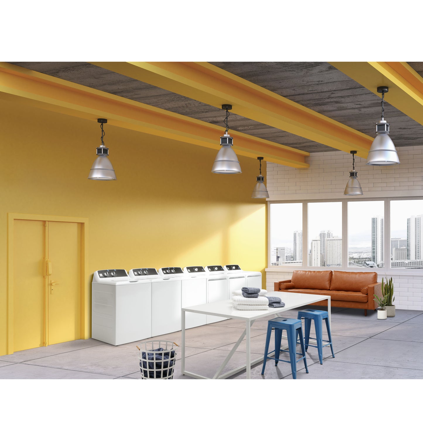 Modern laundry room with white top load washers, yellow walls, concrete floor, orange sofa, and industrial lighting fixtures