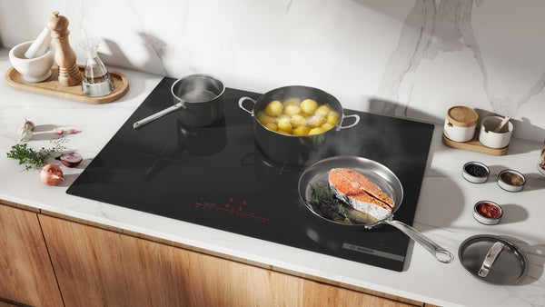 Modern black induction cooktop with three cooking zones, shown with boiling and frying cookware in a kitchen setting