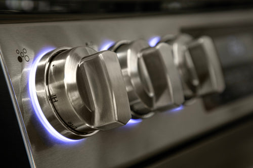 Close-up of stainless steel control knobs with blue LED backlighting on modern gas cooktop in kitchen appliances collection