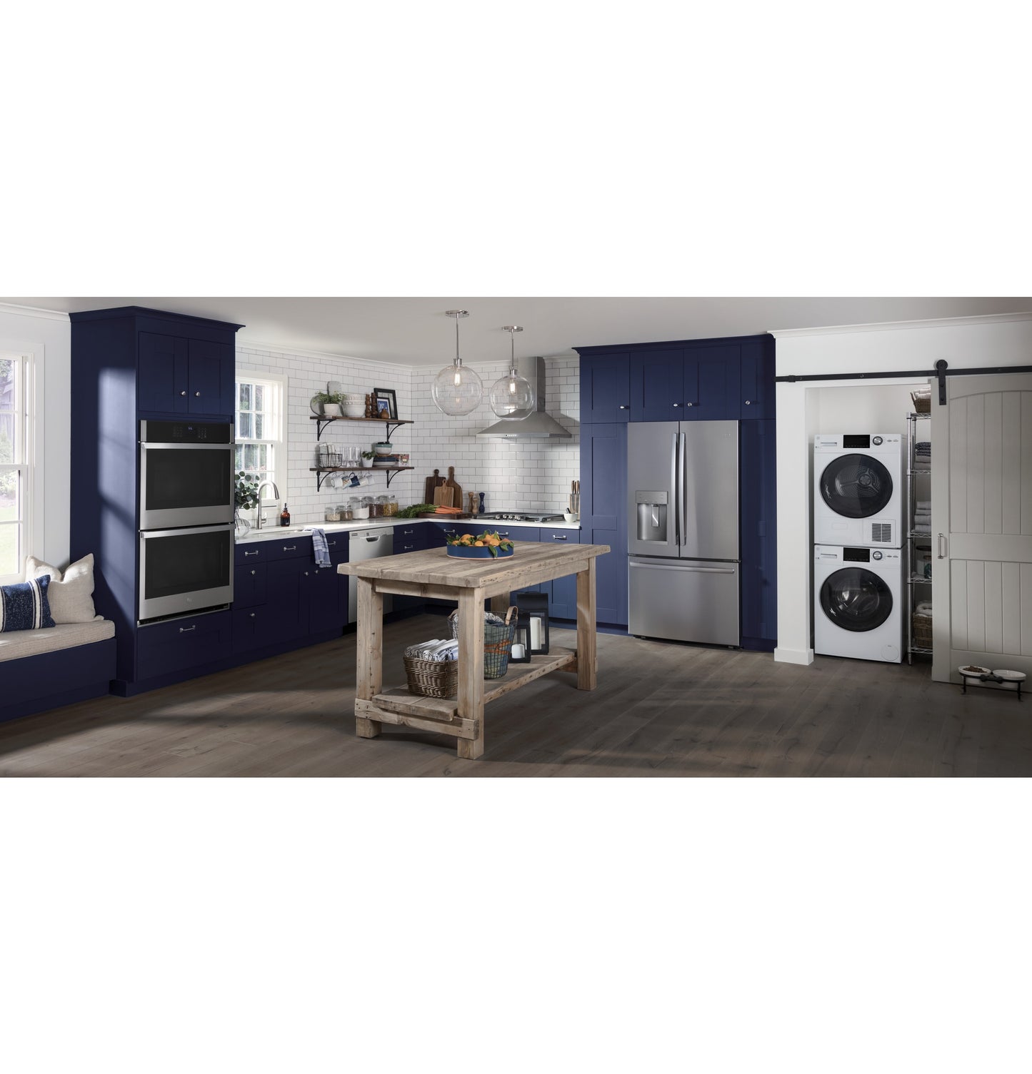 Modern kitchen with navy cabinets, stainless steel appliances, and a stacked white washer and dryer in laundry area
