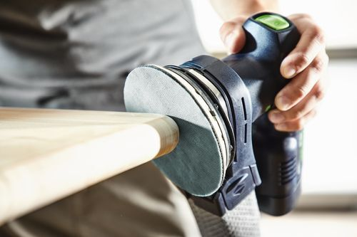Cordless eccentric sander with ergonomic grip and dust collection sanding a wooden surface for home improvement tasks
