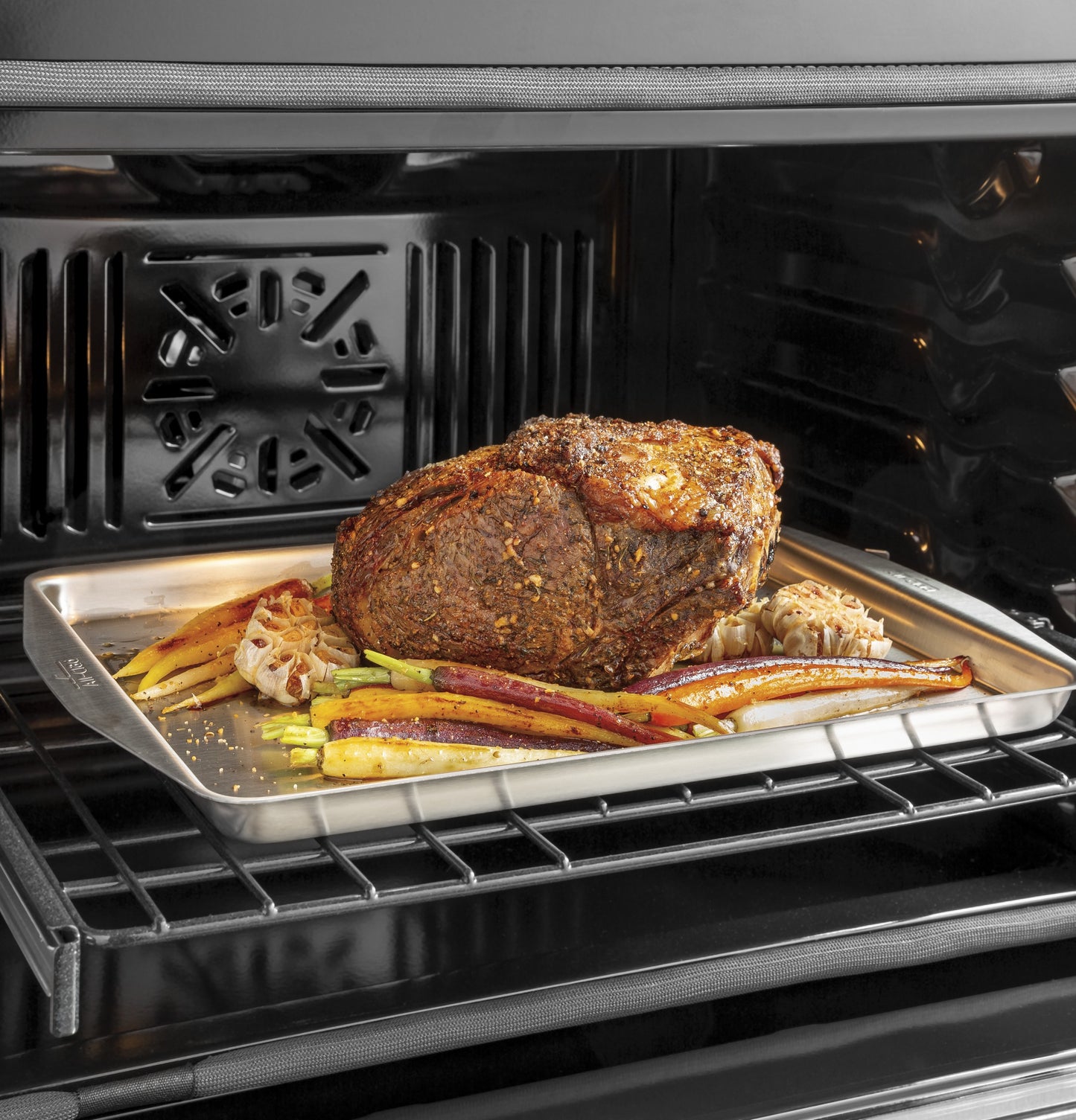 Roast beef with seasoned carrots and garlic cloves cooking on a tray inside a built-in convection wall oven