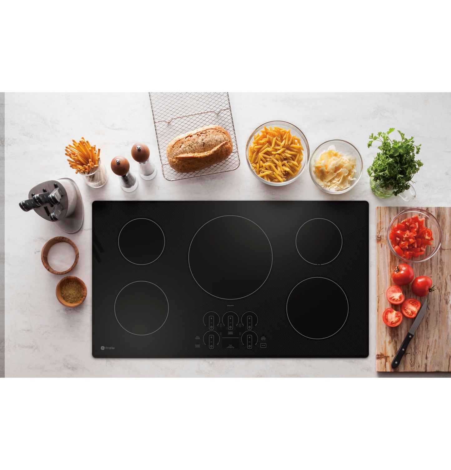 Black touch control induction cooktop with five cooking zones surrounded by kitchen ingredients on countertop
