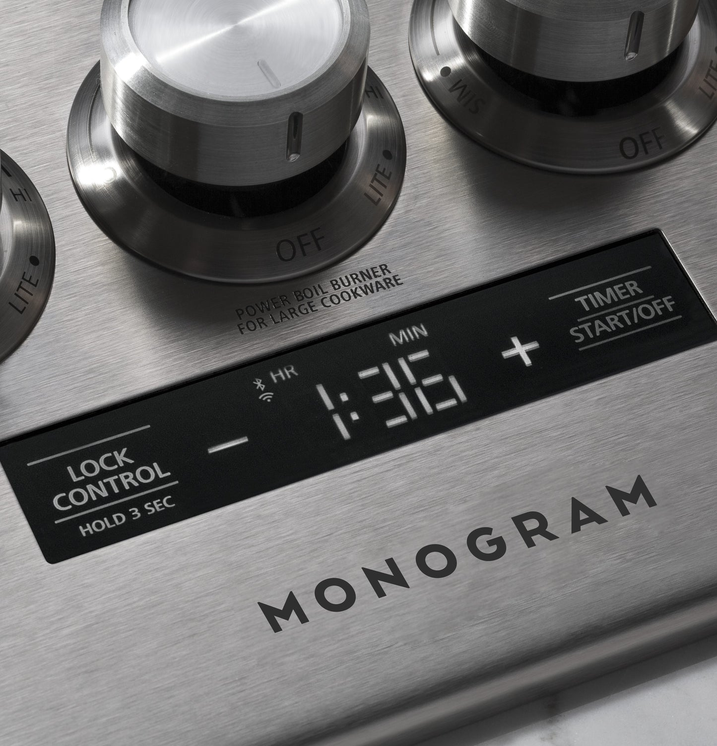 Close-up of stainless steel gas cooktop control panel with digital timer and burner knobs in kitchenware appliances setting