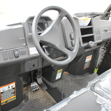 Interior view of a utility vehicle showcasing steering wheel, dashboard controls, and rugged floor mats for outdoor tasks
