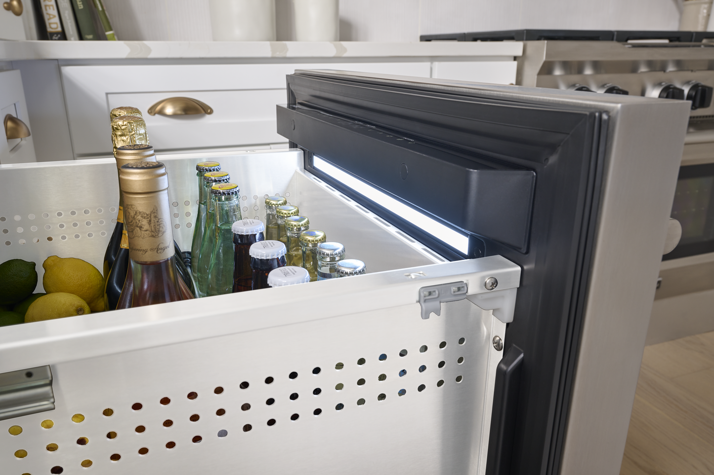 Under-counter stainless steel refrigerator drawer open with beverages inside in modern kitchen setting