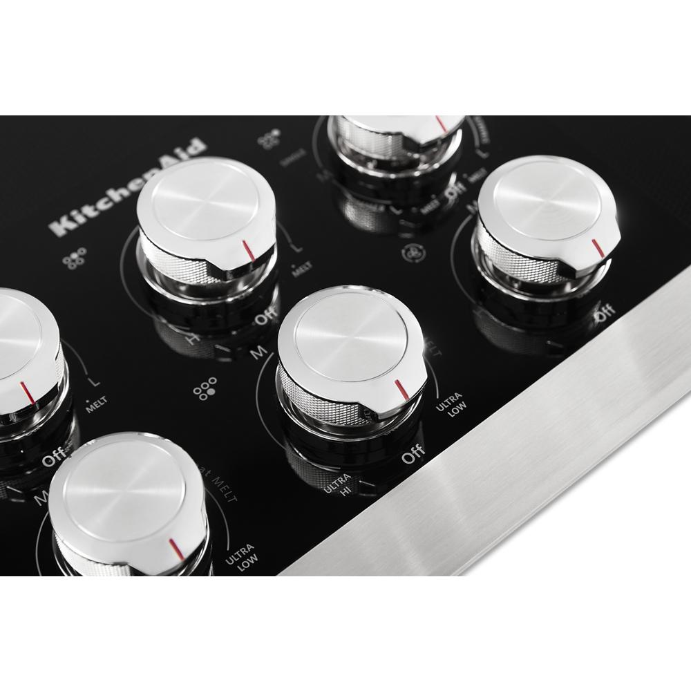 Close-up of stainless steel control knobs on black electric cooktop in KitchenAid appliances and Cooktops collection