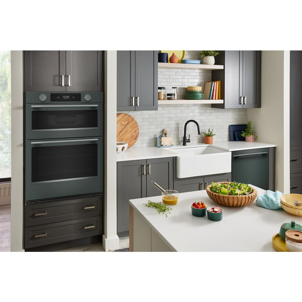 Modern kitchen featuring a Juniper smart electric wall oven integrated into grey cabinetry with farmhouse sink and open shelving