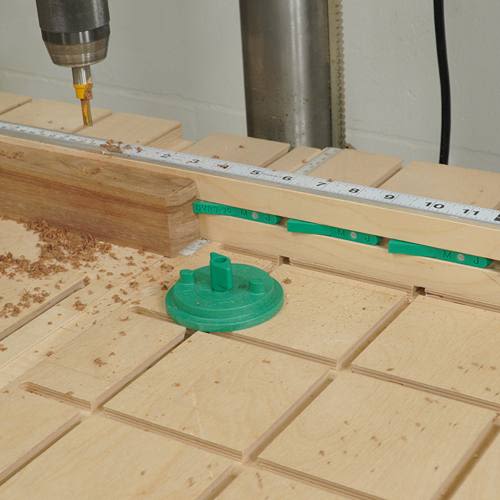 Green plastic stop positioned on slotted wooden workbench beneath measuring ruler for accurate woodworking drilling tasks
