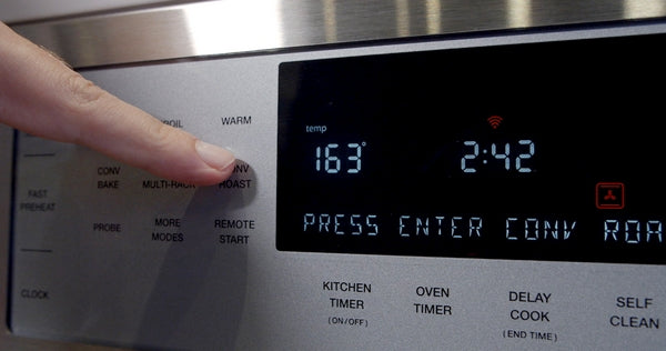Finger pressing multitask baking mode button on stainless steel double wall oven control panel in kitchen appliances collection