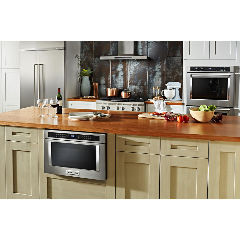 Stainless steel under-counter microwave drawer installed in kitchen island with wood countertop and modern appliances