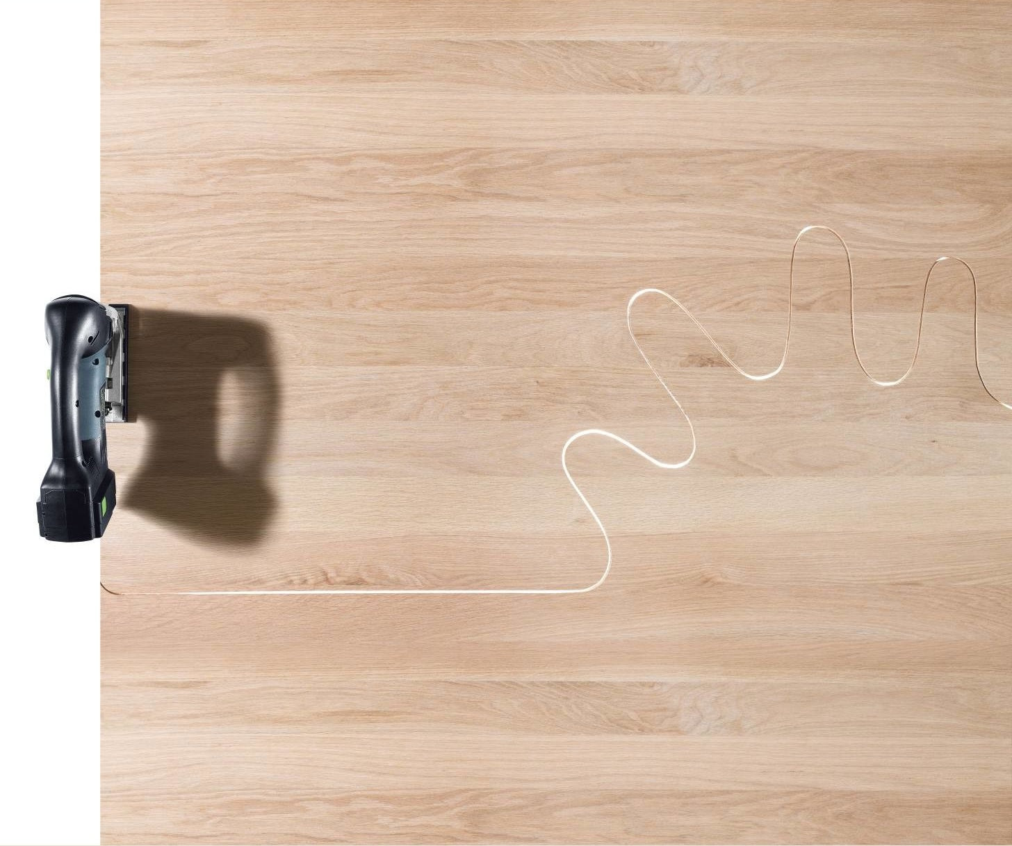 Cordless D-handle jigsaw cutting an intricate curved line on light wood surface in power tools collection