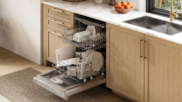 Open 24-inch stainless steel dishwasher with racks loaded with clean dishes in natural wood kitchen setting