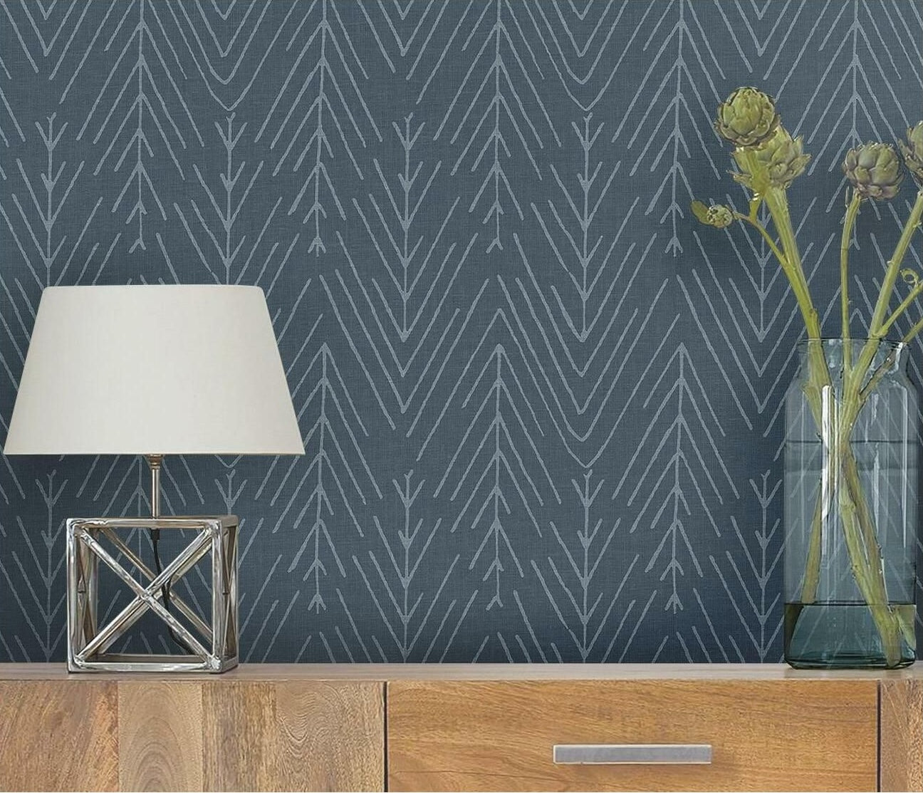 Modern navy wallpaper with twig and herringbone pattern behind wooden dresser, lamp, and glass vase for home decor