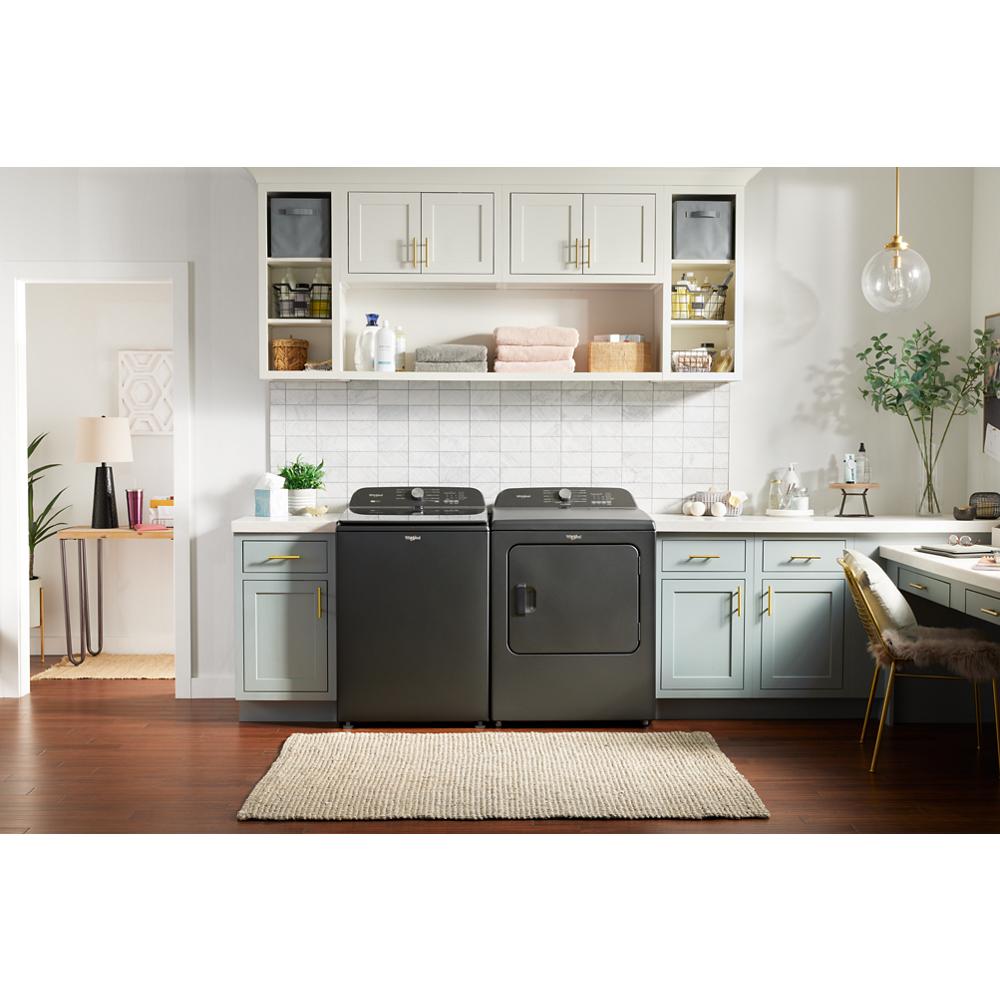 Black Whirlpool washing machine and matching dryer in bright laundry room with blue cabinets and white tile backsplash