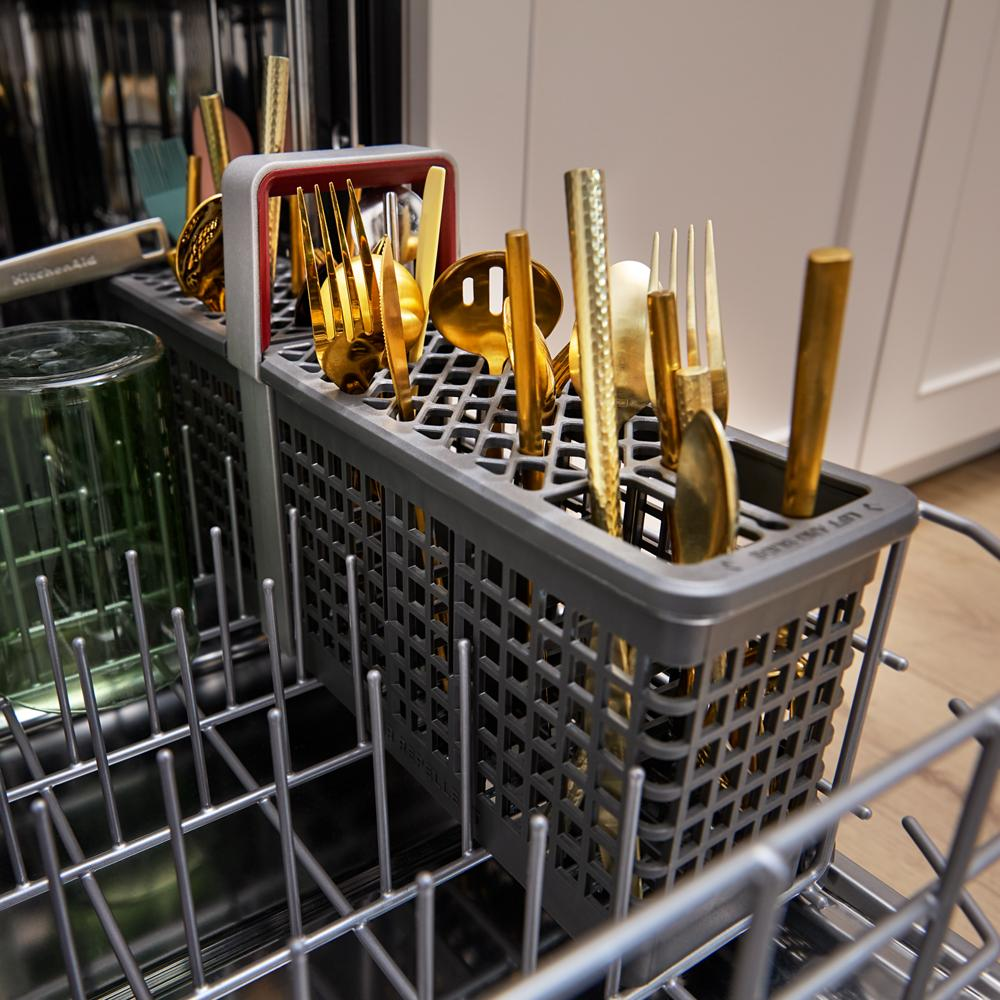 Gray utensil holder with gold-tone flatware and a green glass inside a KitchenAid dishwasher rack