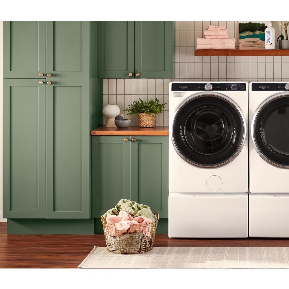 White smart front load washer and dryer set with digital display in kitchen-style laundry room with green cabinets and basket