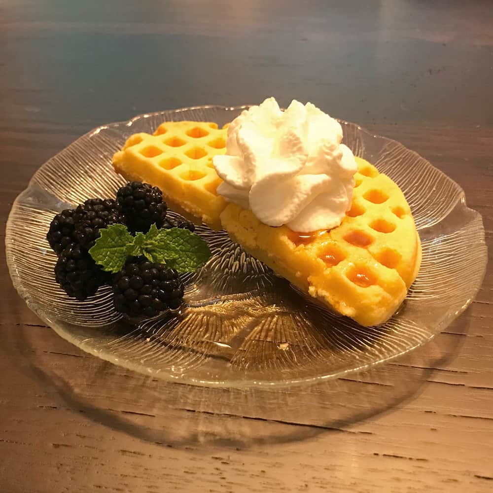 Heart-shaped waffles topped with whipped cream served with blackberries and mint on a clear glass plate