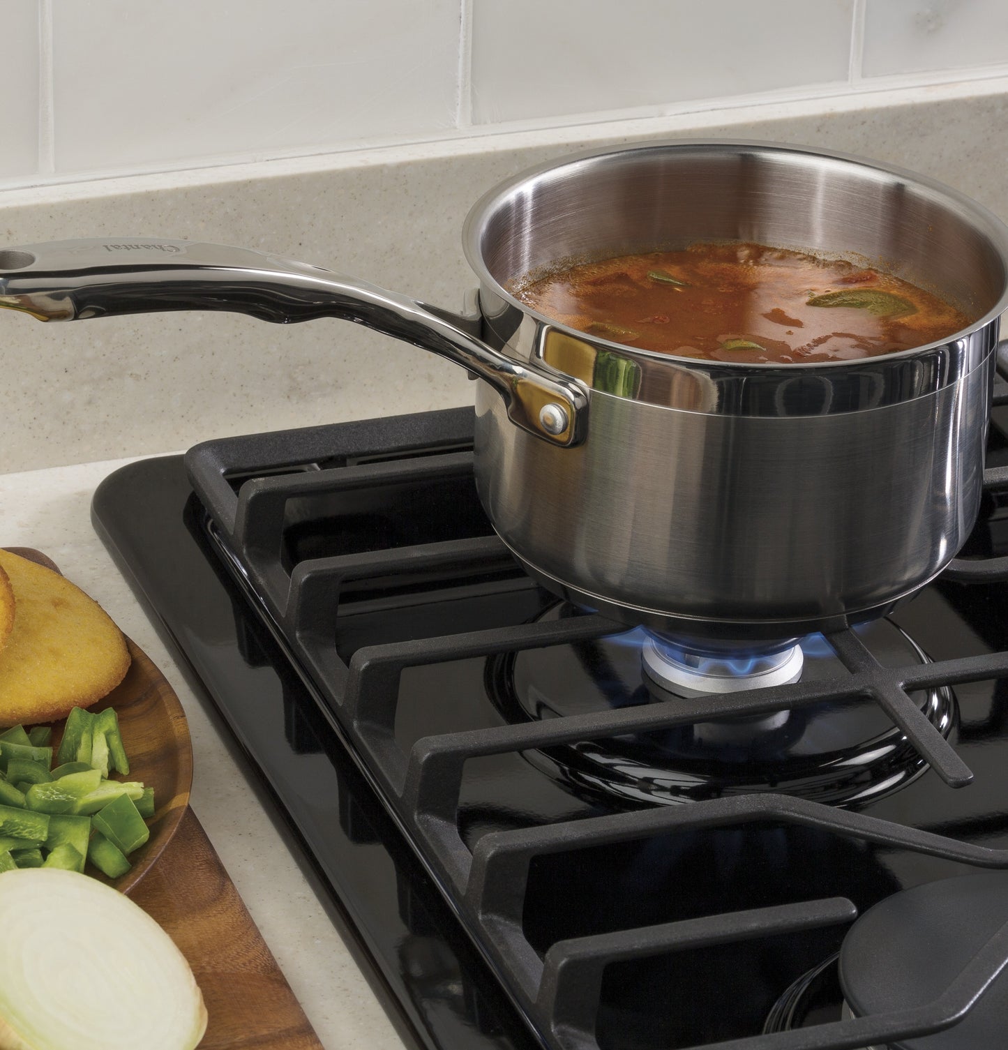 Stainless steel saucepan simmering on black built-in gas cooktop with dishwasher-safe grates in kitchen setting