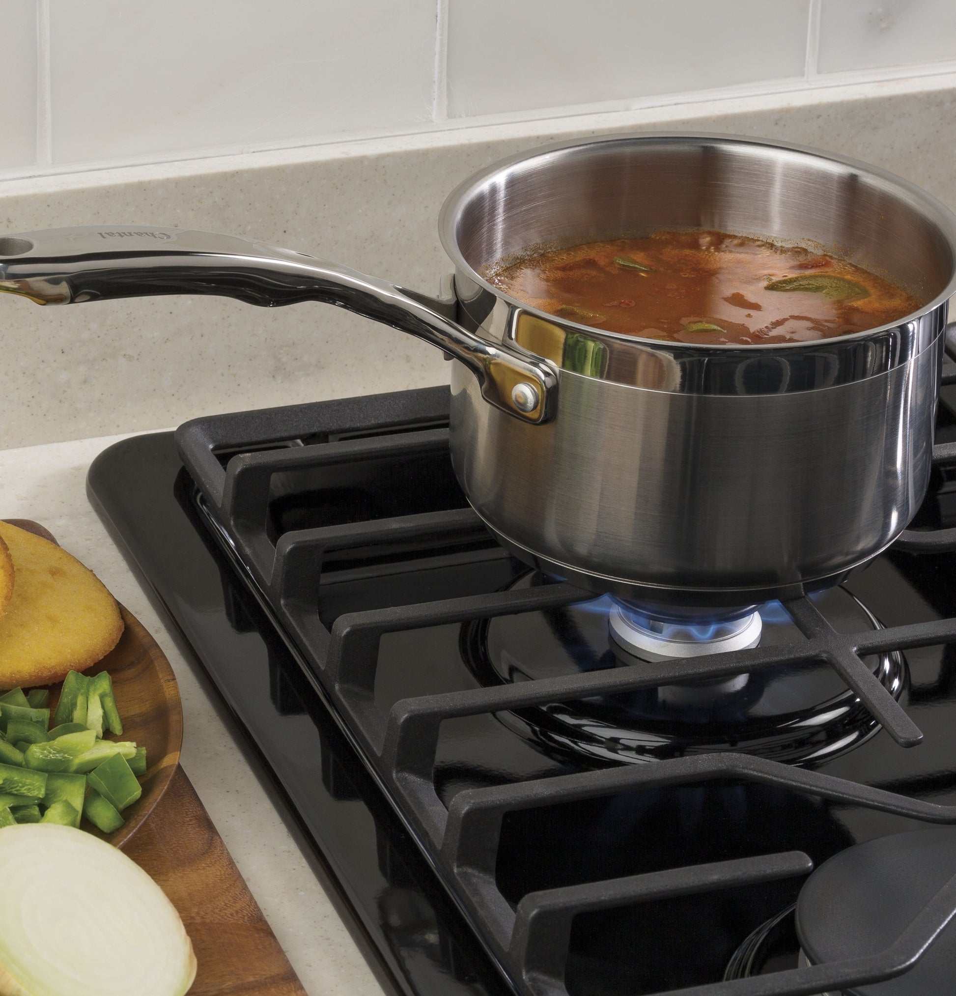 Stainless steel saucepan simmering on black built-in gas cooktop with dishwasher-safe grates in kitchen setting
