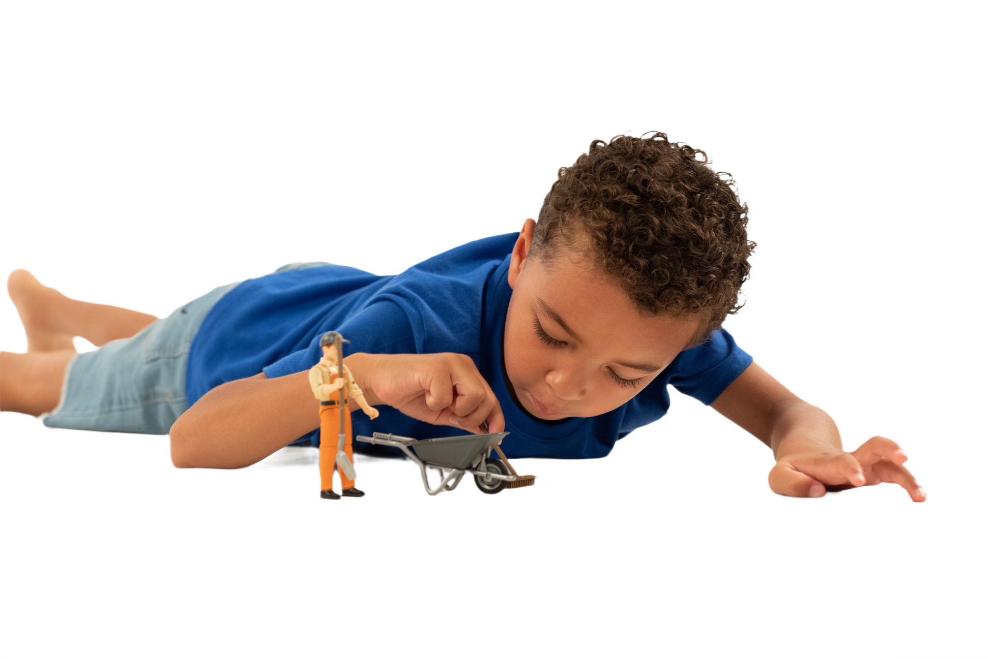 Child lying on floor playing with Bruder municipal worker figure set holding tools and wheelbarrow for imaginative play