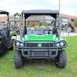 Green utility vehicle with durable frame, off-road tires, and protective canopy parked on grass near equipment displays