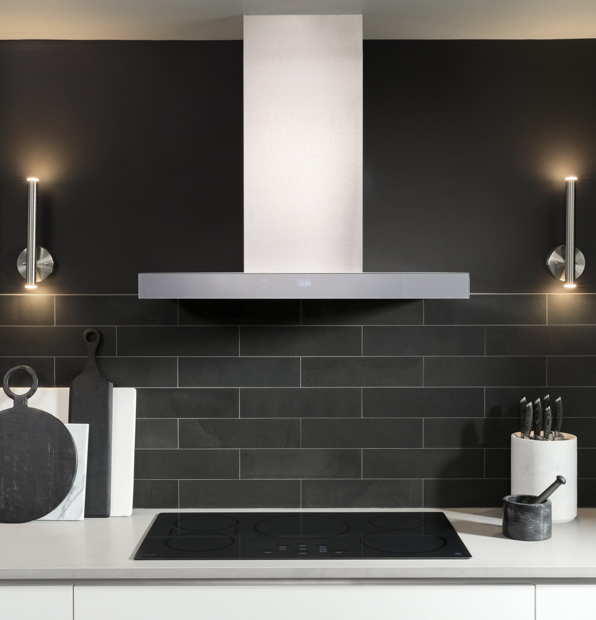 Sleek wall mount stainless steel hood with perimeter venting above black glass cooktop in modern kitchen setting