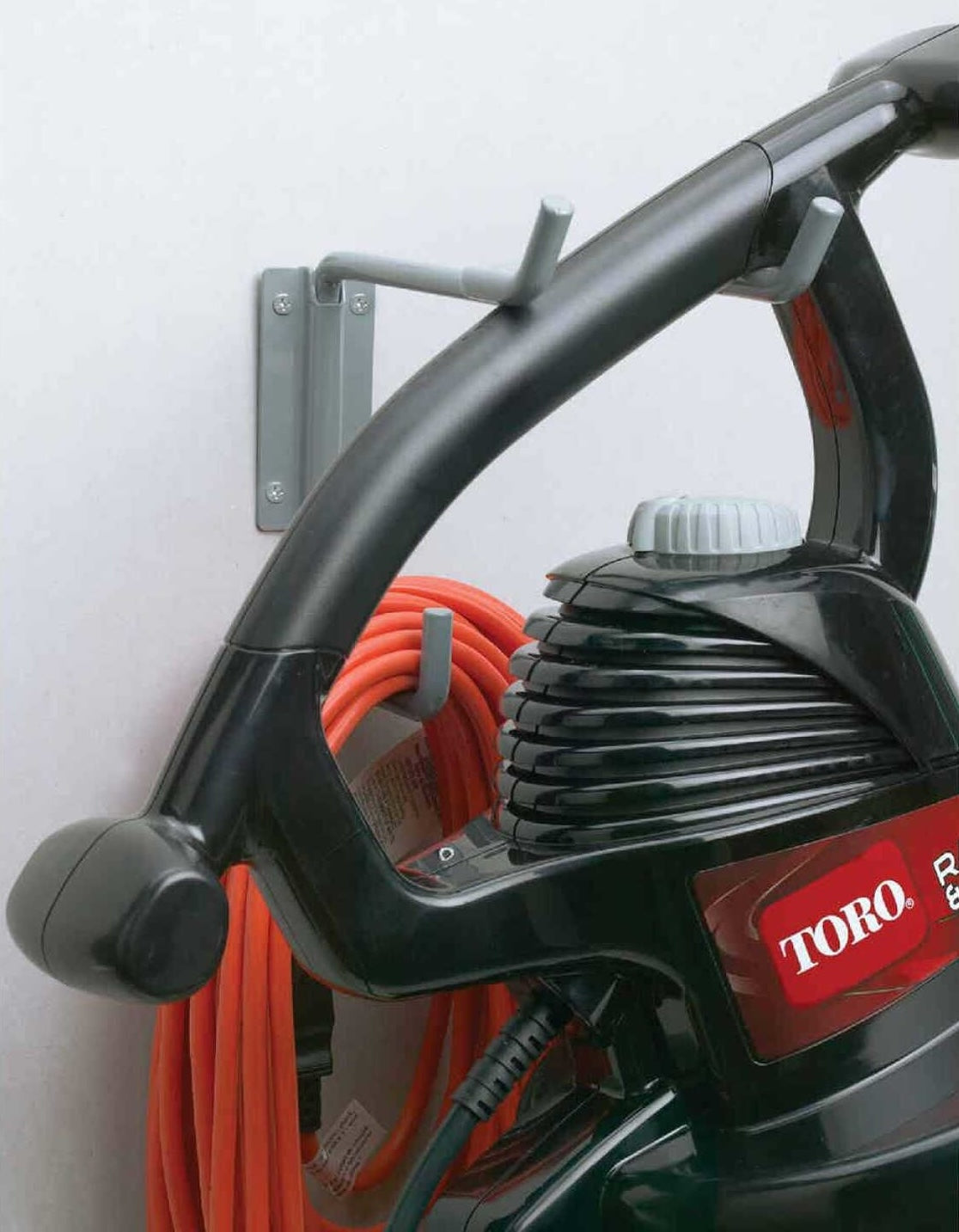 Gray wire utility hanger mounted on wall holding a black garden power tool and orange extension cord in garage storage setting