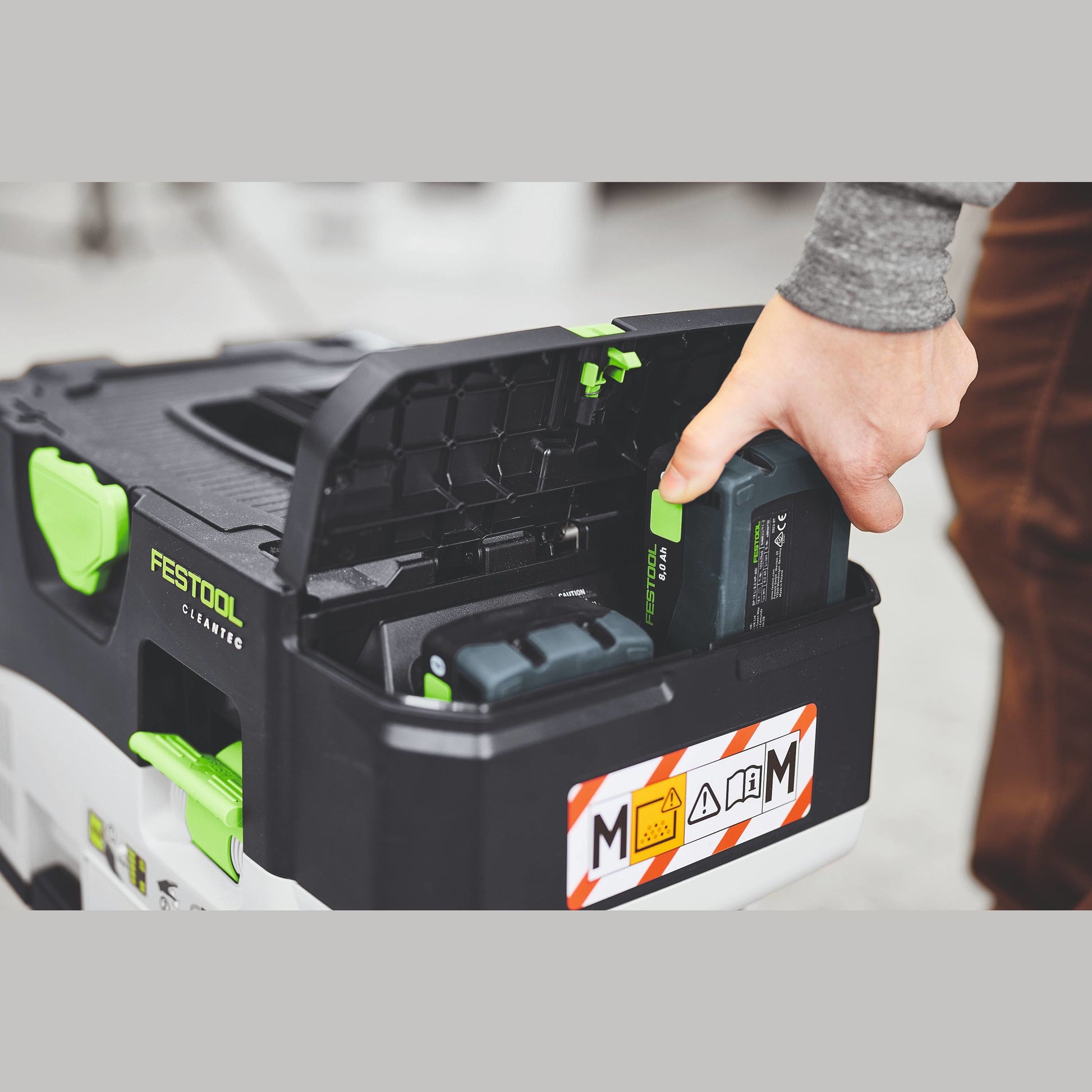 Hand placing a rechargeable Festool 18V 8.0 Ah battery pack into black tool storage box for home improvement tasks