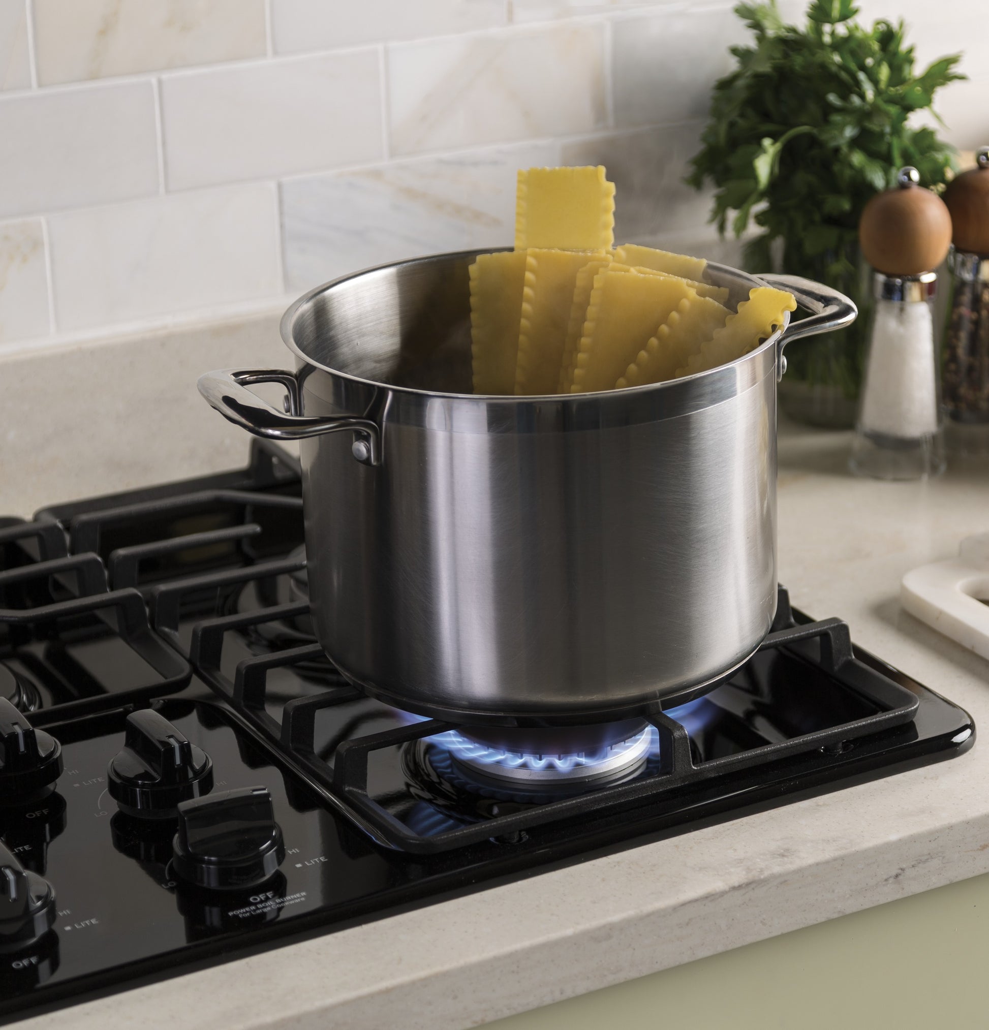 Stainless steel pot with uncooked pasta on a burner of a black built-in gas cooktop in Kitchen & Kitchenware collections