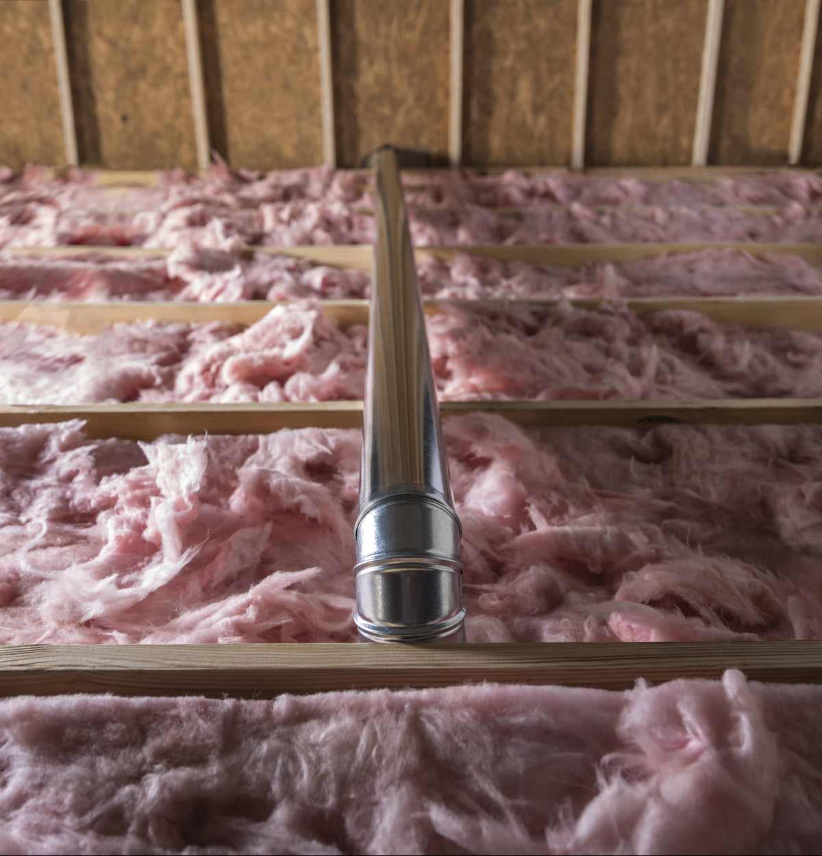 Silver dryer vent duct running over pink fiberglass insulation between wooden ceiling joists in home improvement setting