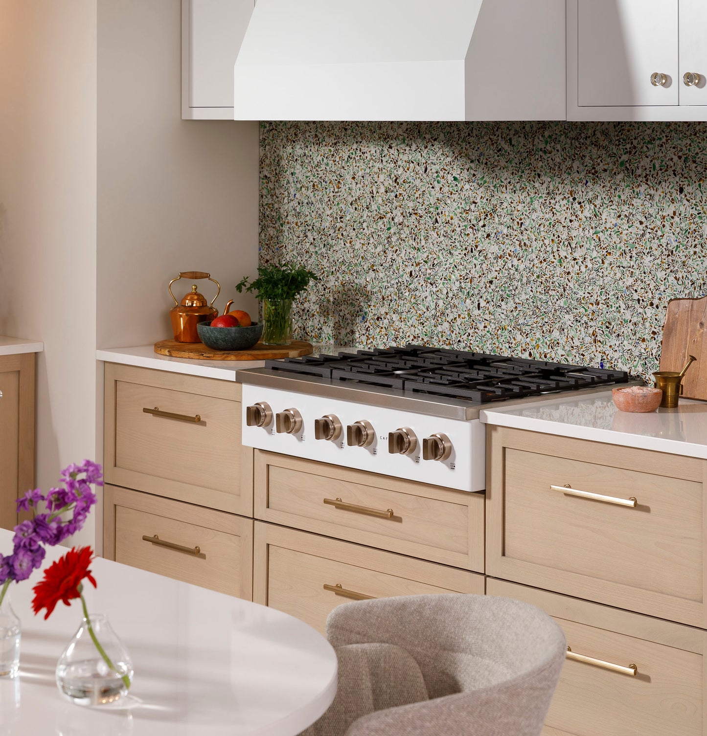 Modern kitchen with light wood cabinetry featuring a six-burner commercial-style gas rangetop and terrazzo backsplash