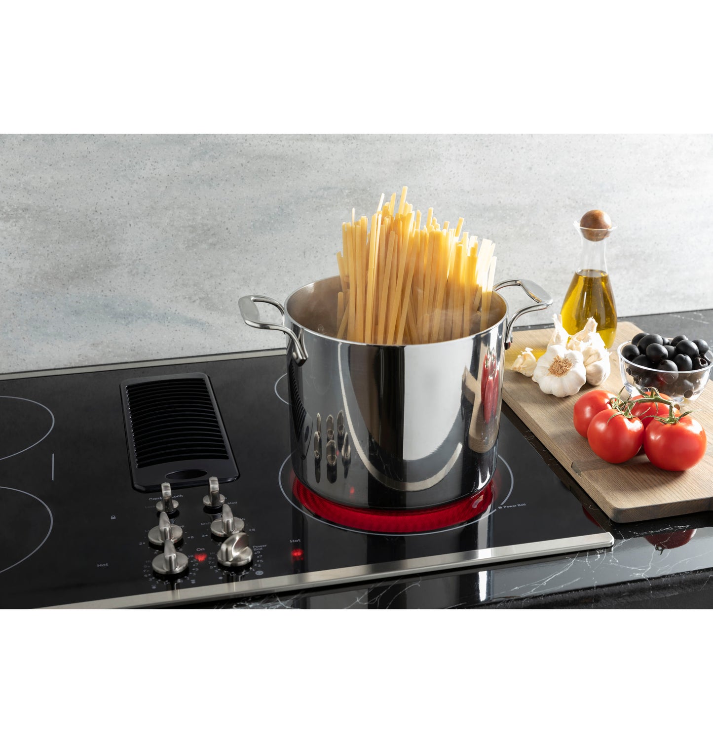 Stainless steel pot with uncooked spaghetti heating on active red coil of GE Profile downdraft electric cooktop