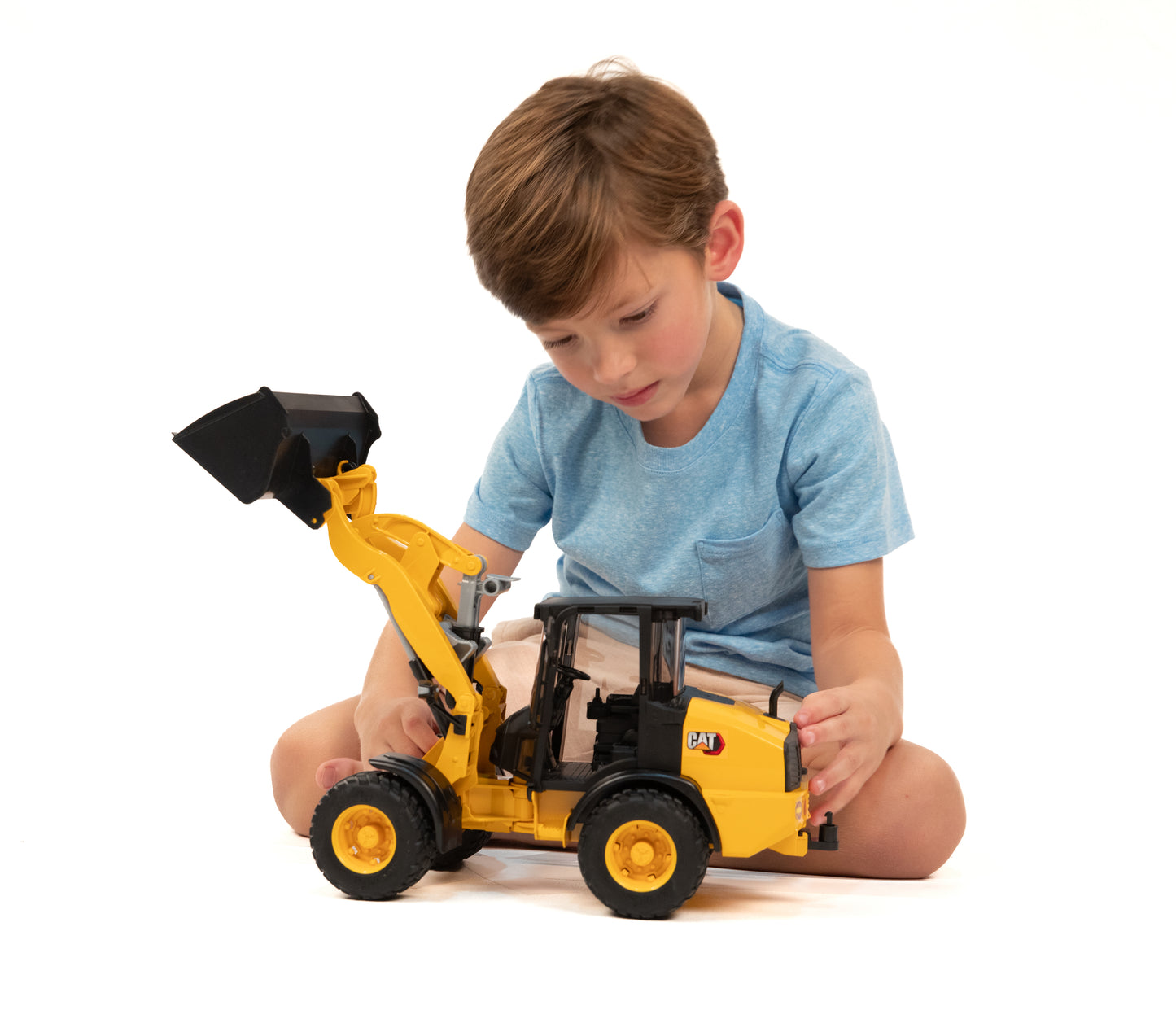 Child engaged in imaginative play with yellow Bruder CAT construction toy in tools and home improvement setting