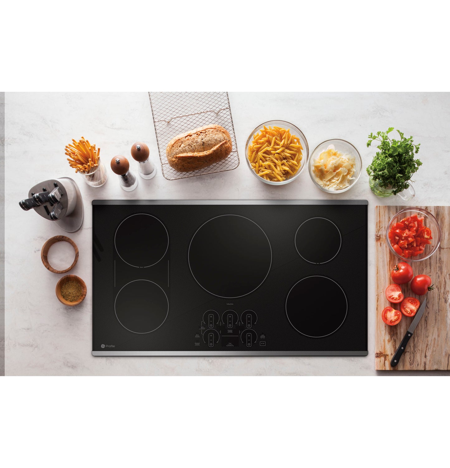 Sleek black built-in induction cooktop with five cooking zones and touch controls surrounded by fresh ingredients and kitchen tools