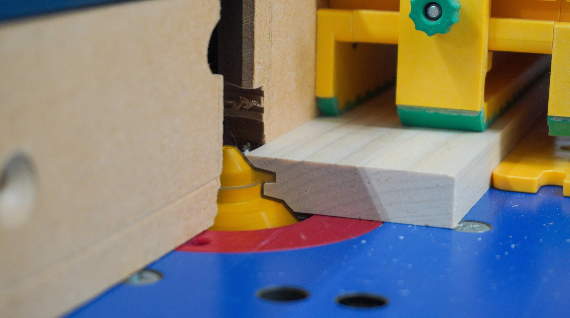 Close-up of yellow and red woodworking bit cutting precise lock miter joint on light wood board in workshop tool setup