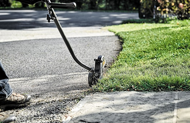 Power head fitted with split boom attachment trimming grass edges near driveway in outdoor home improvement tools collection