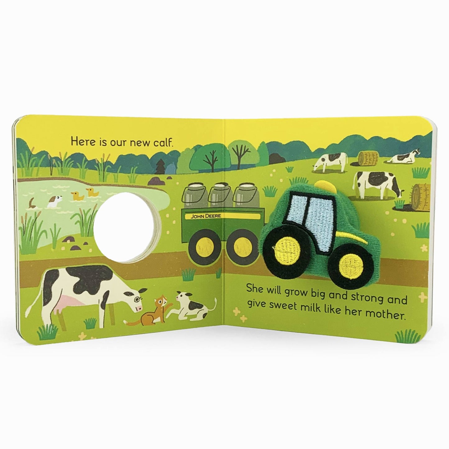 Children’s board book spread with fabric John Deere tractor patch and illustrated farm scene with cows and pond