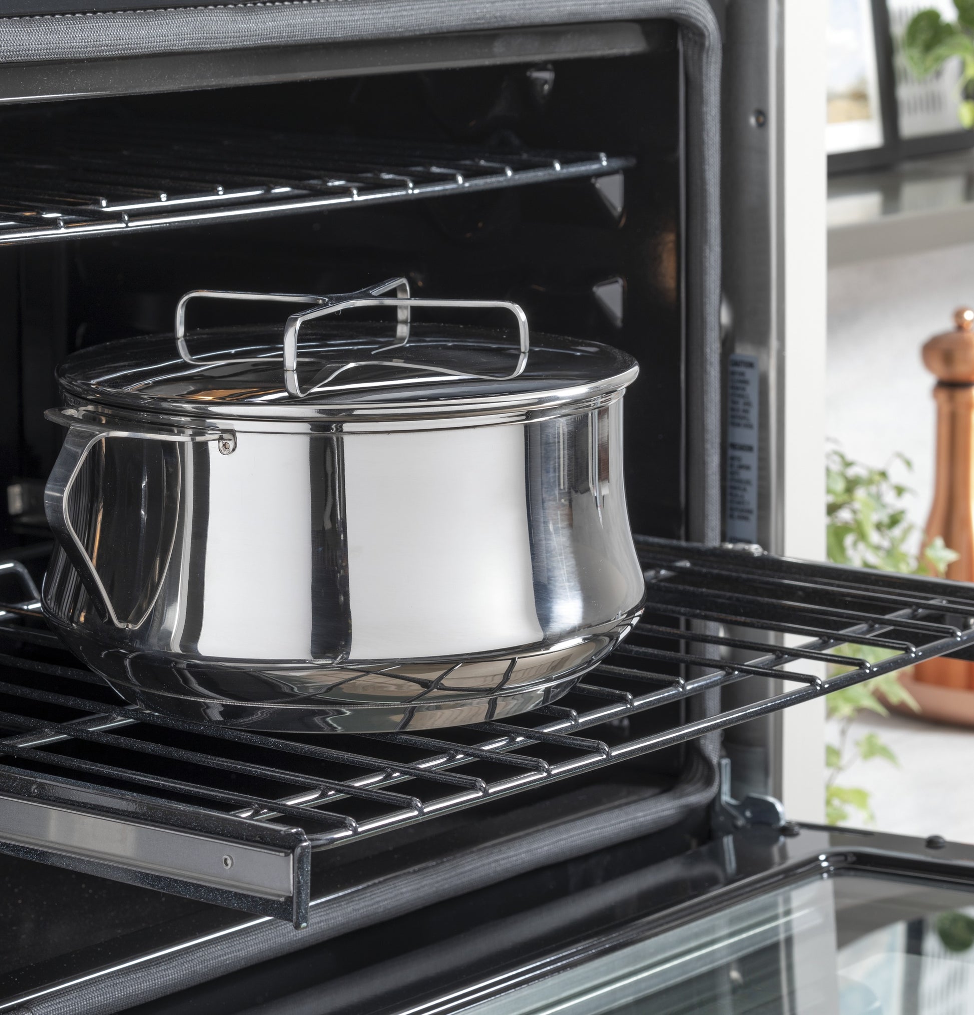 Stainless steel pot with lid inside open black built-in wall oven rack in modern kitchen and kitchenware setting