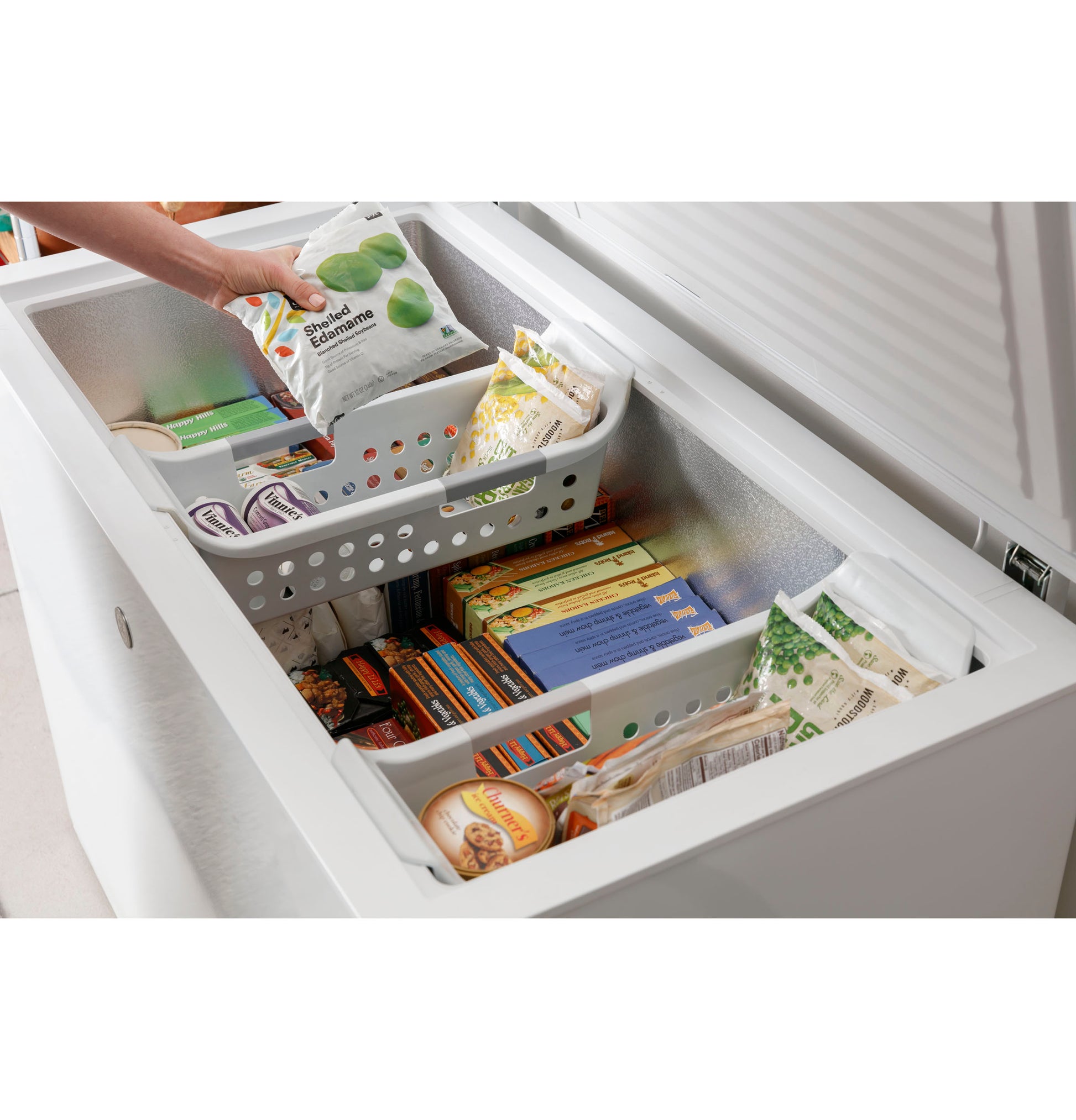 Open white chest freezer filled with organized frozen food items and plastic baskets for storage in kitchen appliance setting