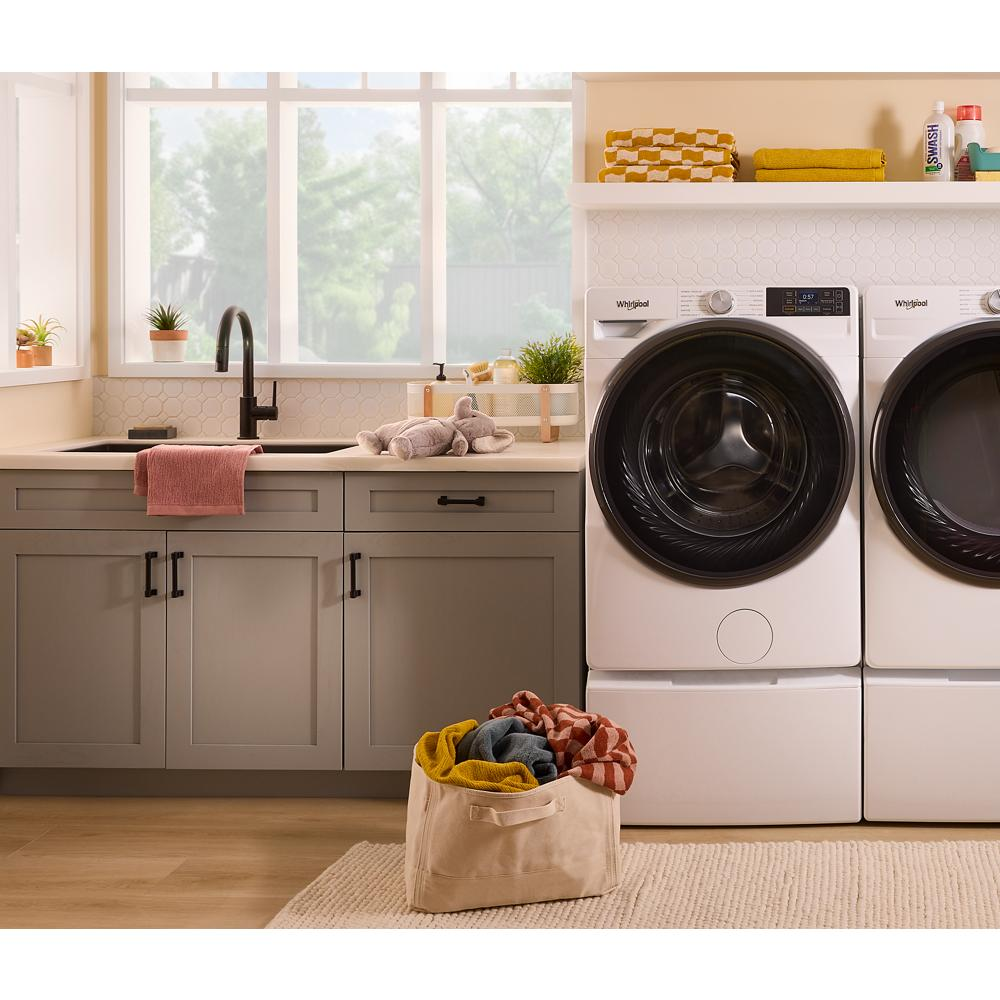 White front load washers and dryers with digital displays in a bright laundry room featuring gray cabinets and natural light