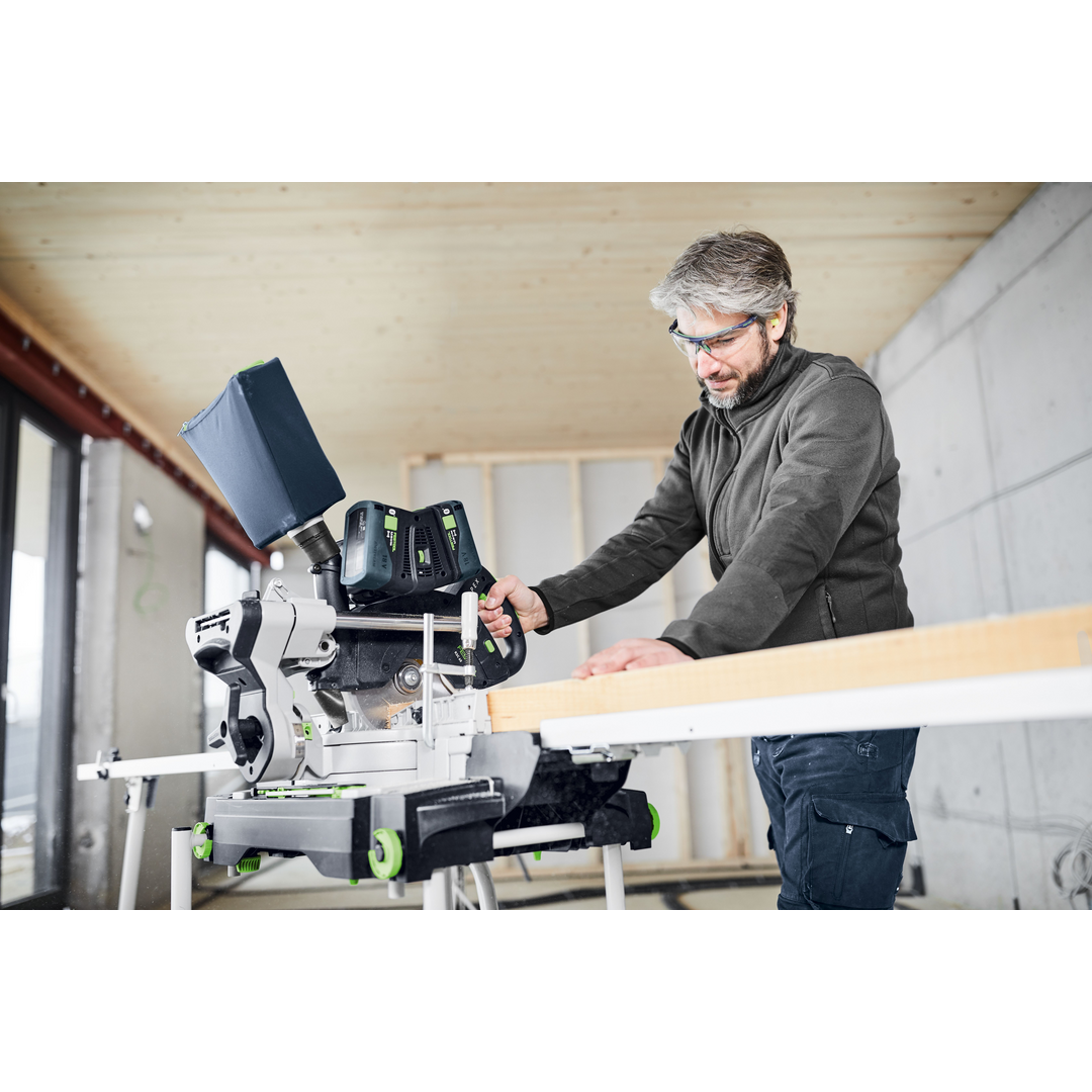 Man using a cordless compound miter saw in a woodworking workshop with safety glasses and dark clothing